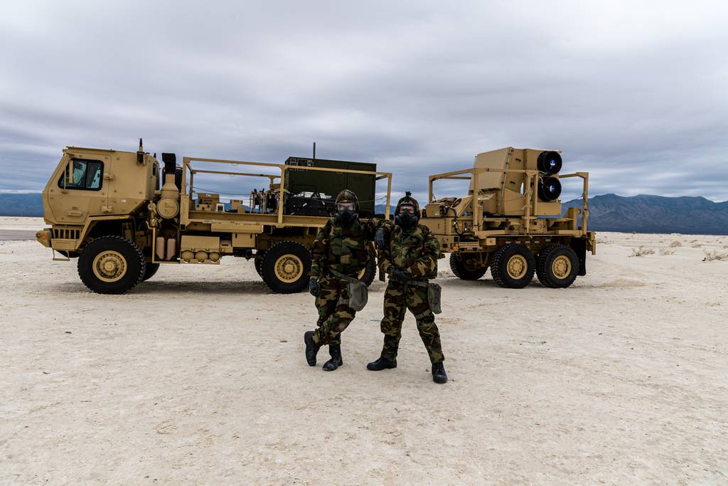 U.S. Army Cpl. Jordan Wierzbicki, left, and Spc. Daemon Vann pose in front of a Sentinel A4 sensor while clad in chemical protective gear.